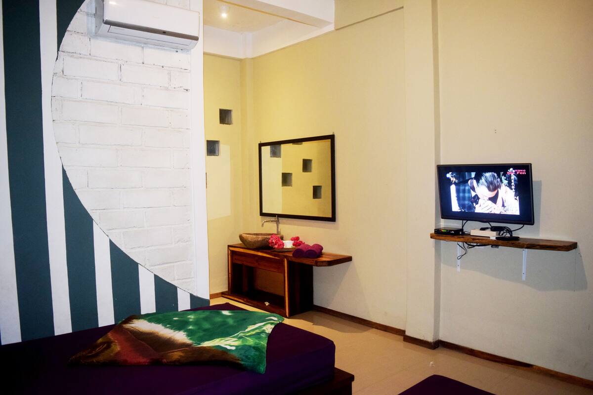 A modern room with a bed, a television, a small sink, and a mirror.