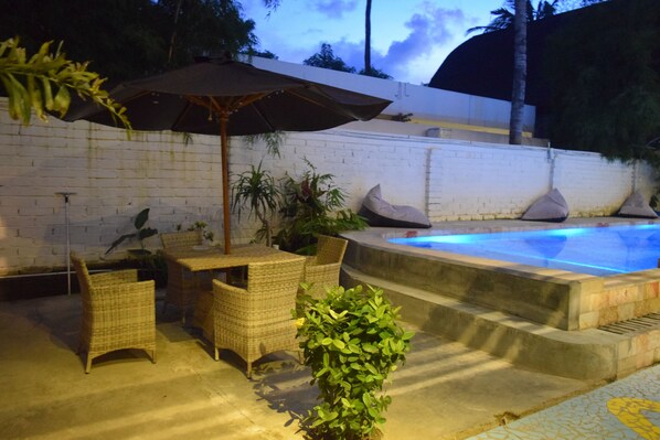 A poolside area with wicker furniture, a potted plant, and a tiled floor. - Panda Cottage - Hostel (Gili Trawangan)