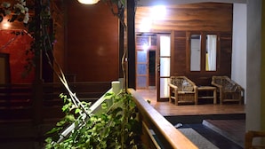 A wooden interior with a staircase, a seating area with wicker chairs, and a view into another room. - Panda Cottage - Hostel (Gili Trawangan)