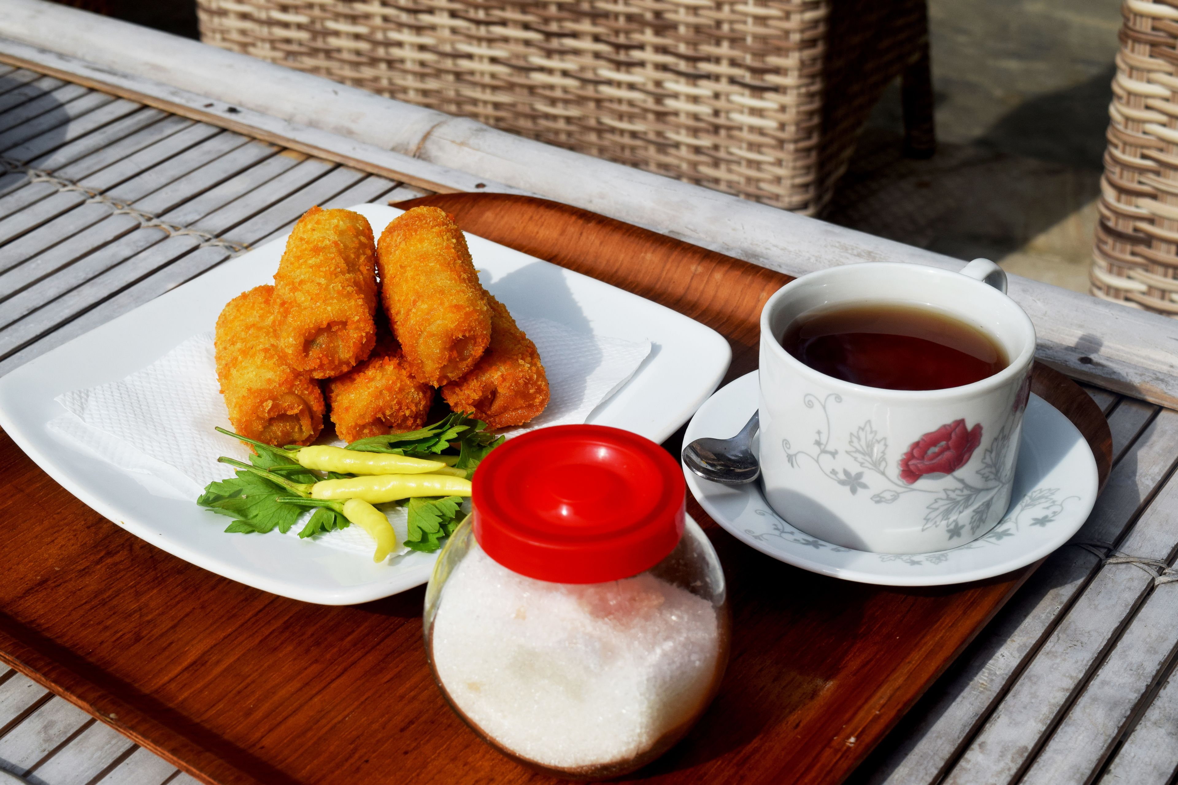 A tray with fried food, a cup of tea, and a salt shaker.