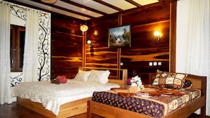 A wooden bed with a patterned bedspread, a nightstand with a lamp, and a painting on the wall. - Panda Cottage - Hostel (Gili Trawangan)