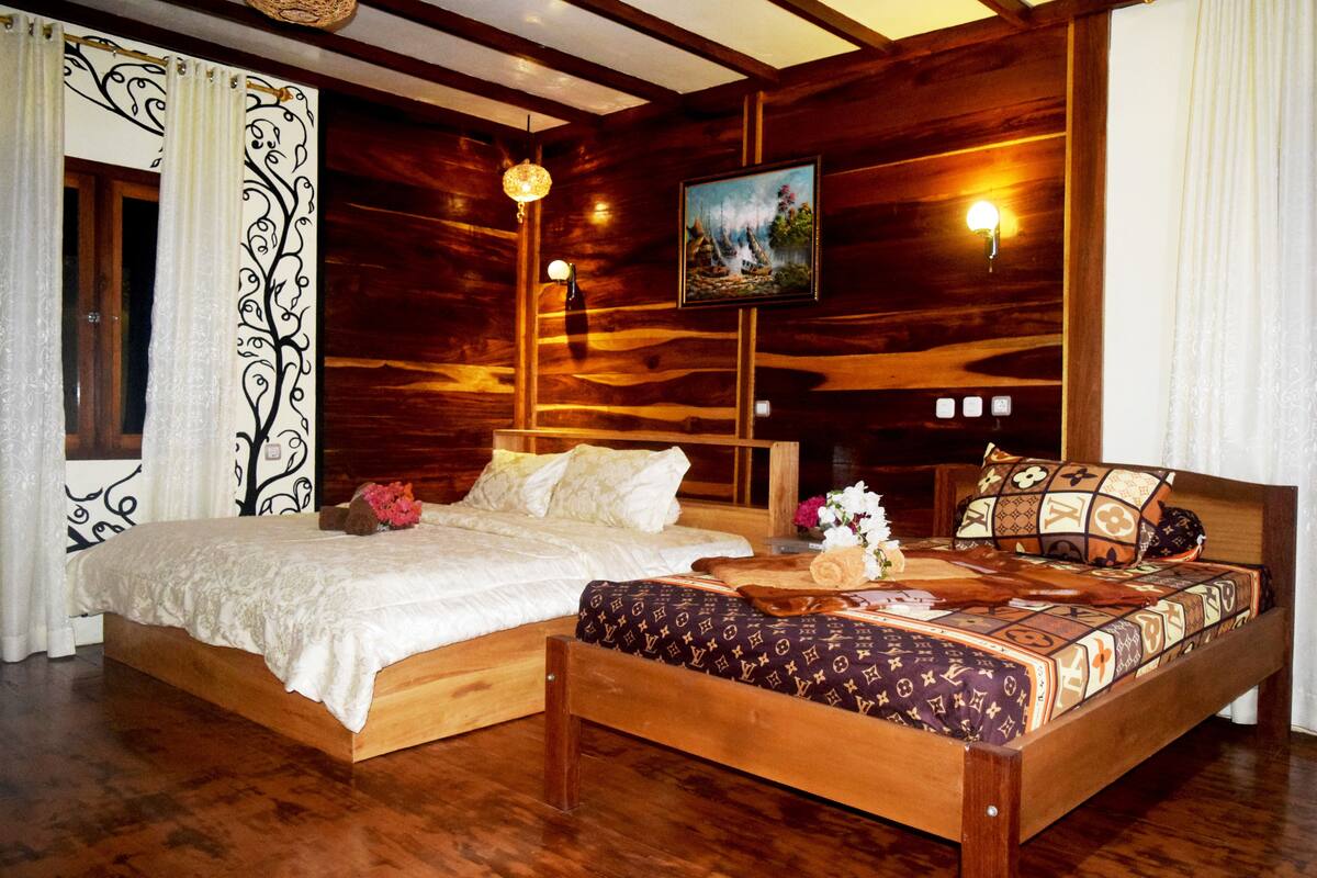 A wooden bed with a patterned bedspread, a nightstand with a lamp, and a painting on the wall.