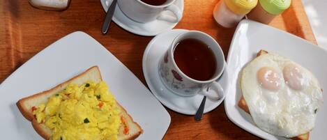 A tray with scrambled eggs on toast, a fried egg, and two cups of tea, along with condiments.