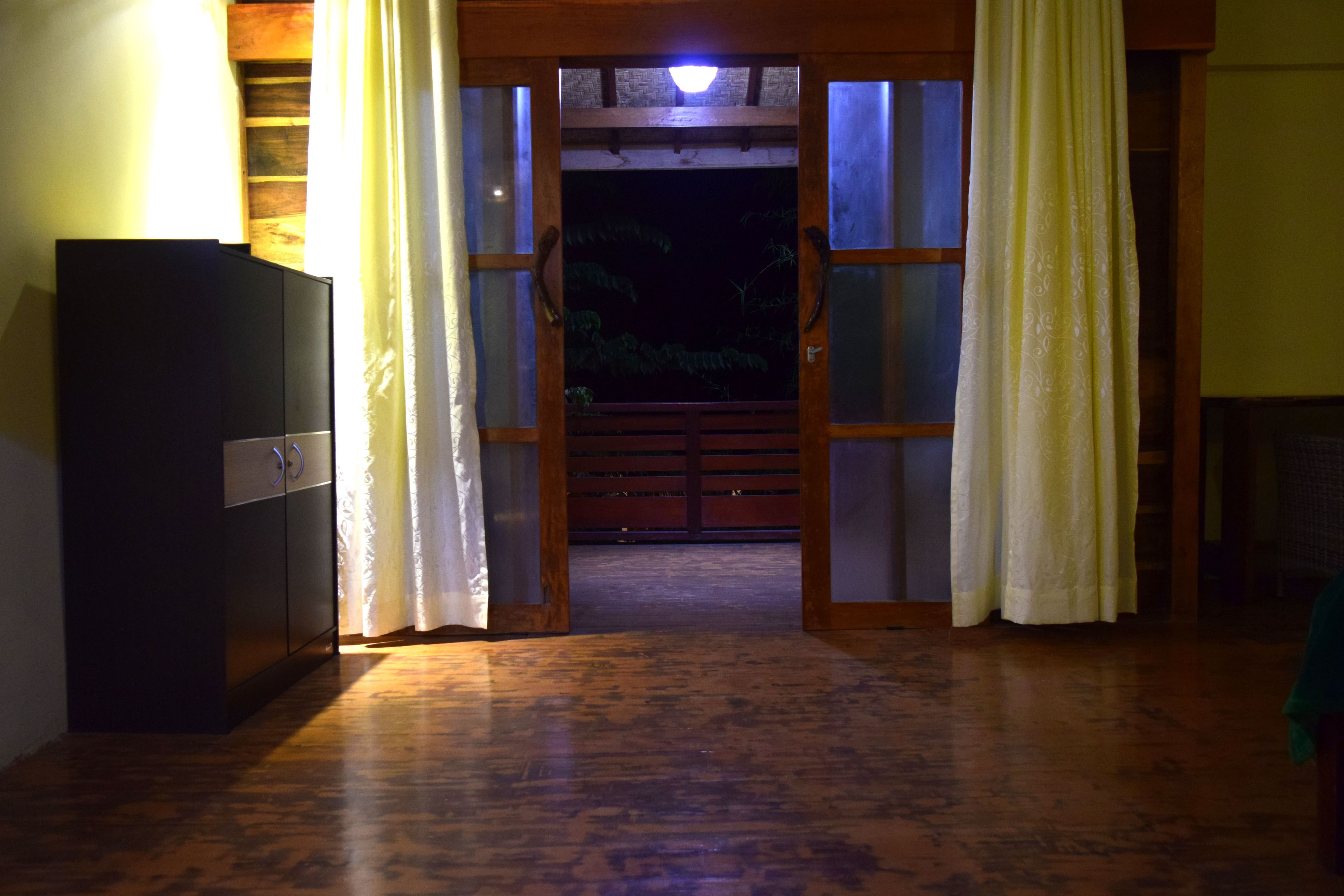 A hallway with wooden flooring leading to a dark outdoor area through a doorway with curtains.