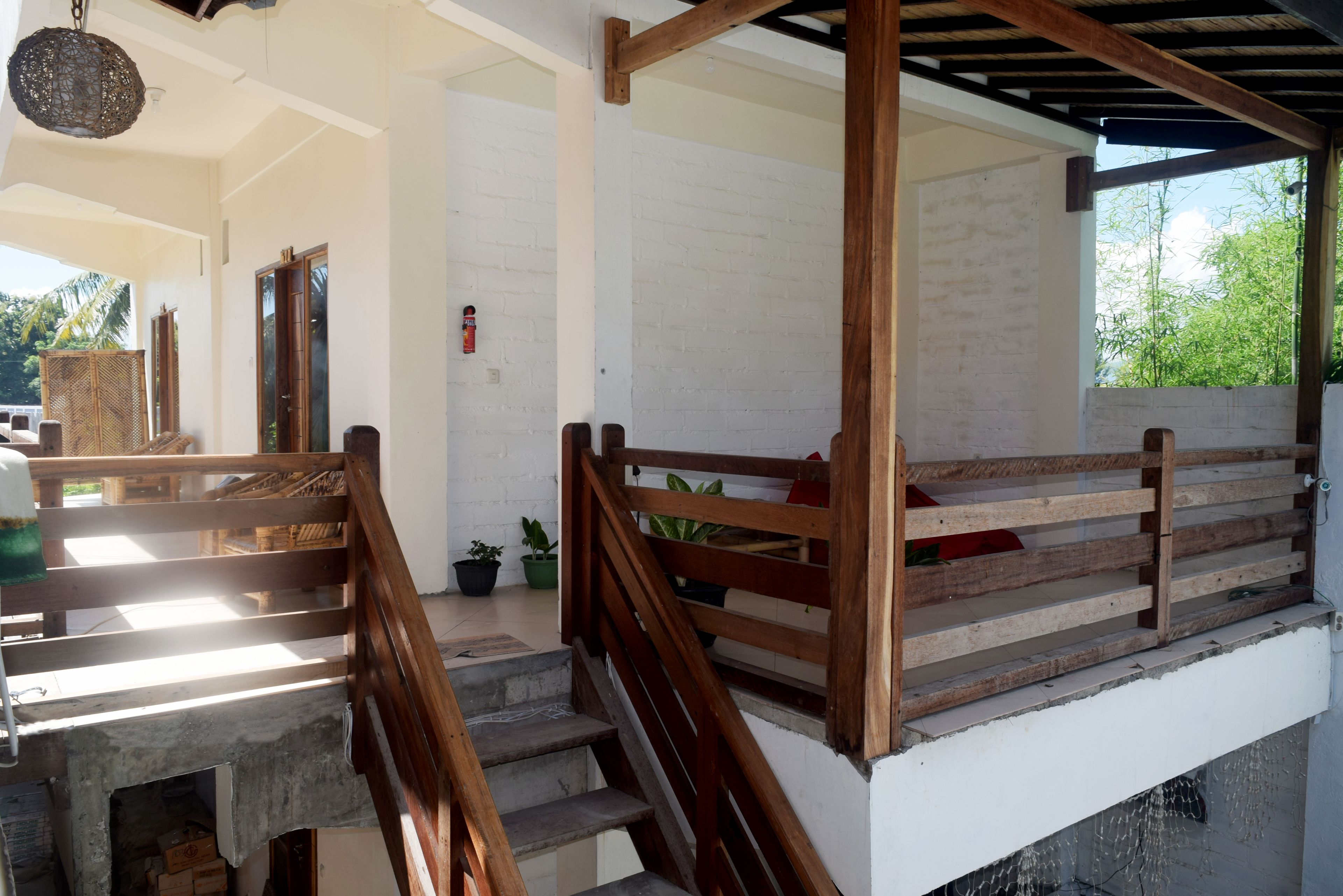A staircase with wooden railings leading to a covered area with a white brick wall and a view of greenery outside.