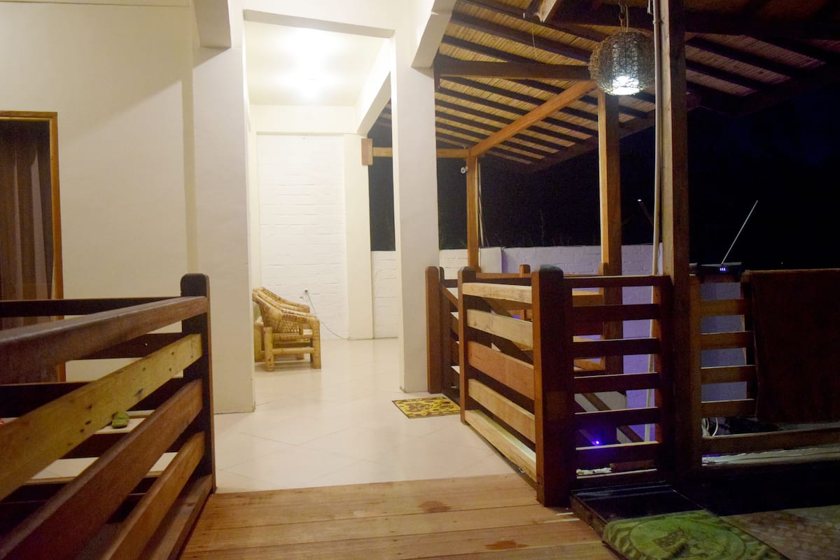 A wooden-fenced balcony with a view of the night sky, a hanging light fixture, and a laptop on a table.
