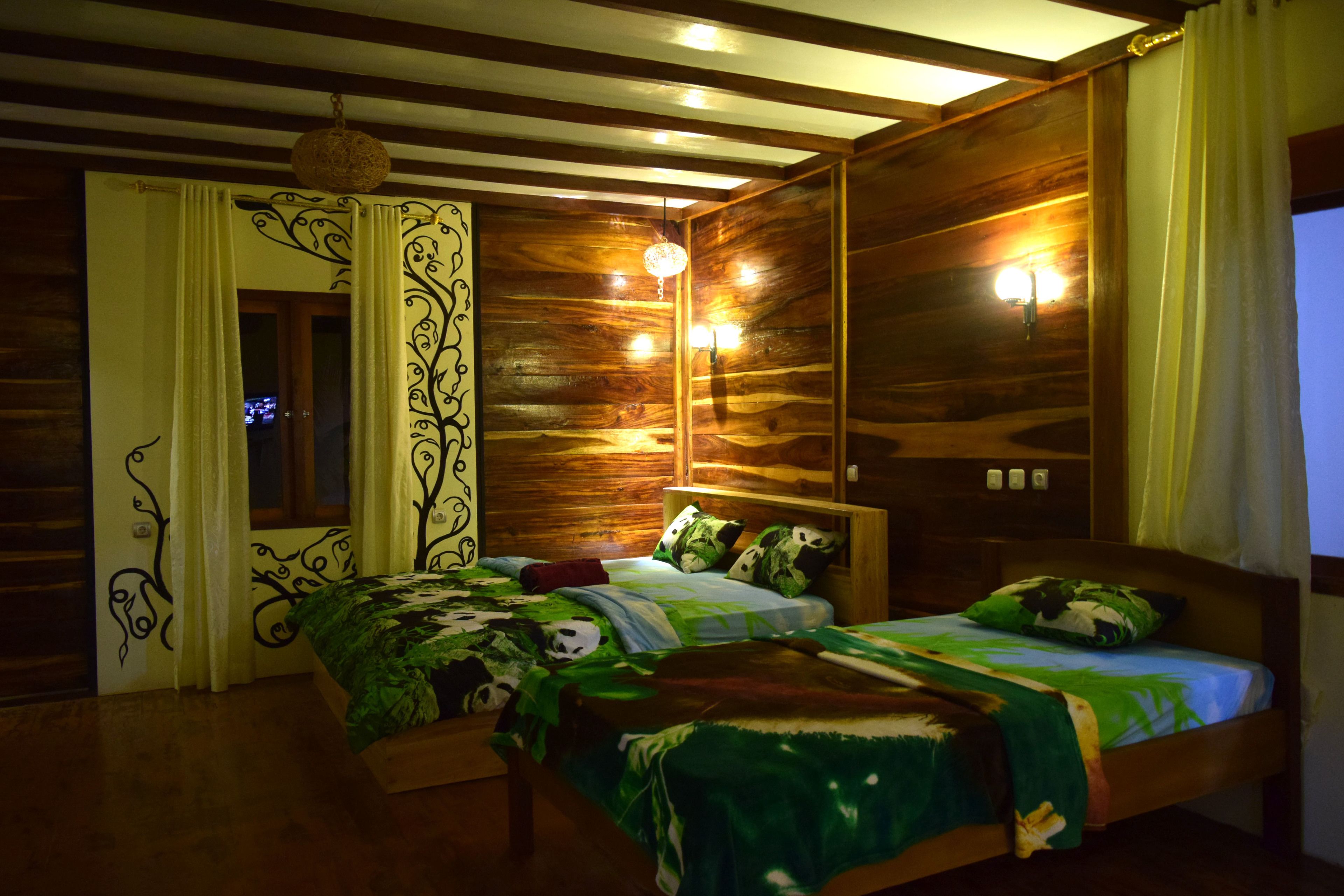 A wooden-paneled bedroom with two beds, a hanging light fixture, and a window with curtains.