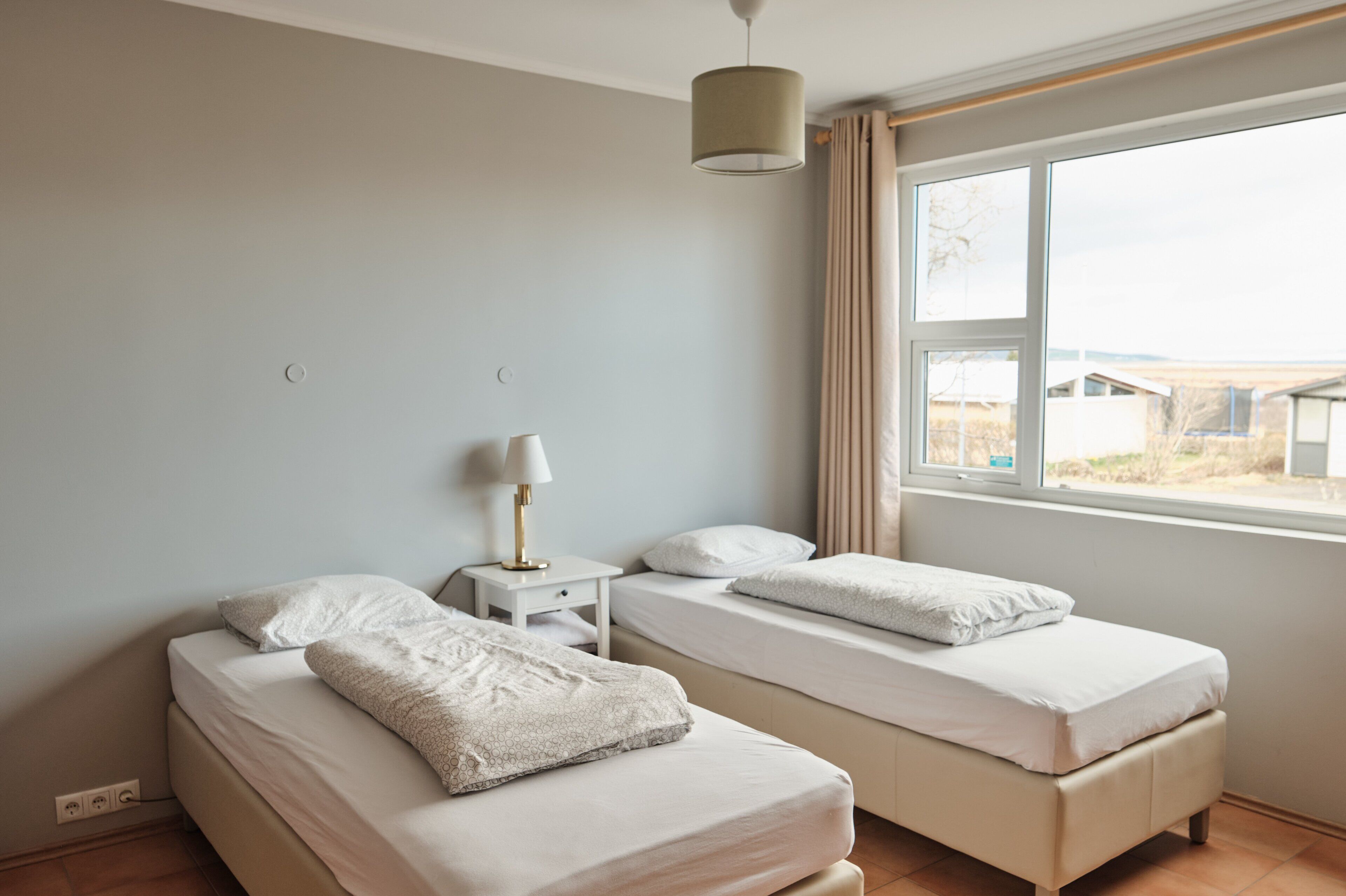 Une chambre avec deux lits, une table de chevet, une lampe et une fenêtre avec des rideaux.