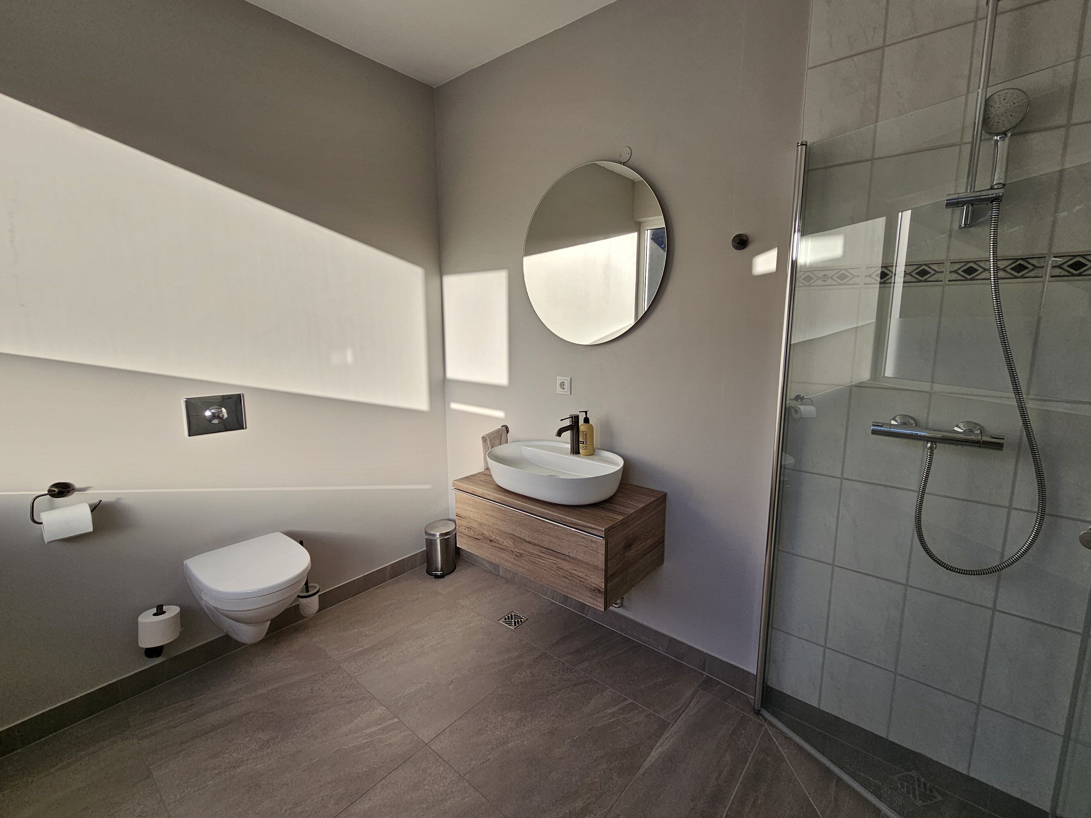 Un baño moderno con inodoro, lavamanos, espejo y ducha.