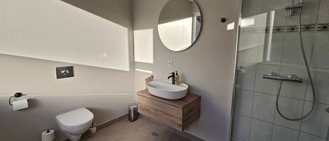 Un baño moderno con inodoro, lavamanos, espejo y ducha.