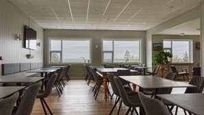 Un comedor amplio con varias mesas y sillas, ventanas grandes con vistas y una planta en maceta.