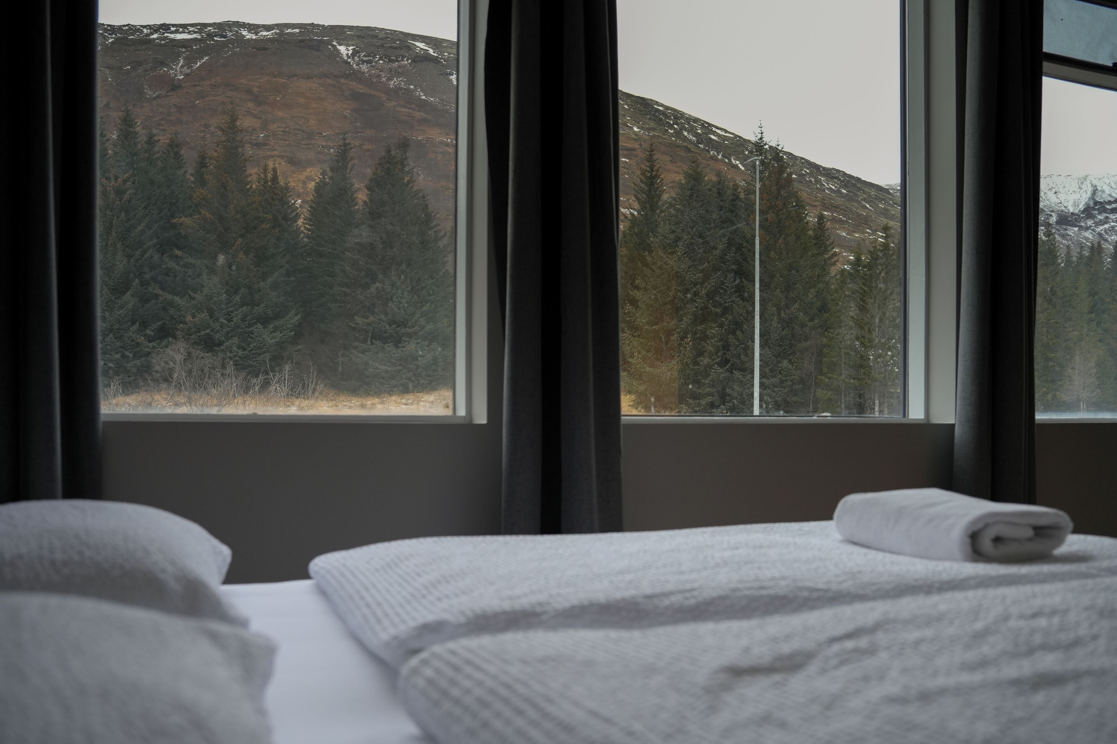 A hotel room with a bed, a window, and a view of a forest and mountains.