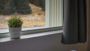 Una ventana con vistas a un paisaje montañoso, una planta en maceta y una toalla doblada sobre una cama.
