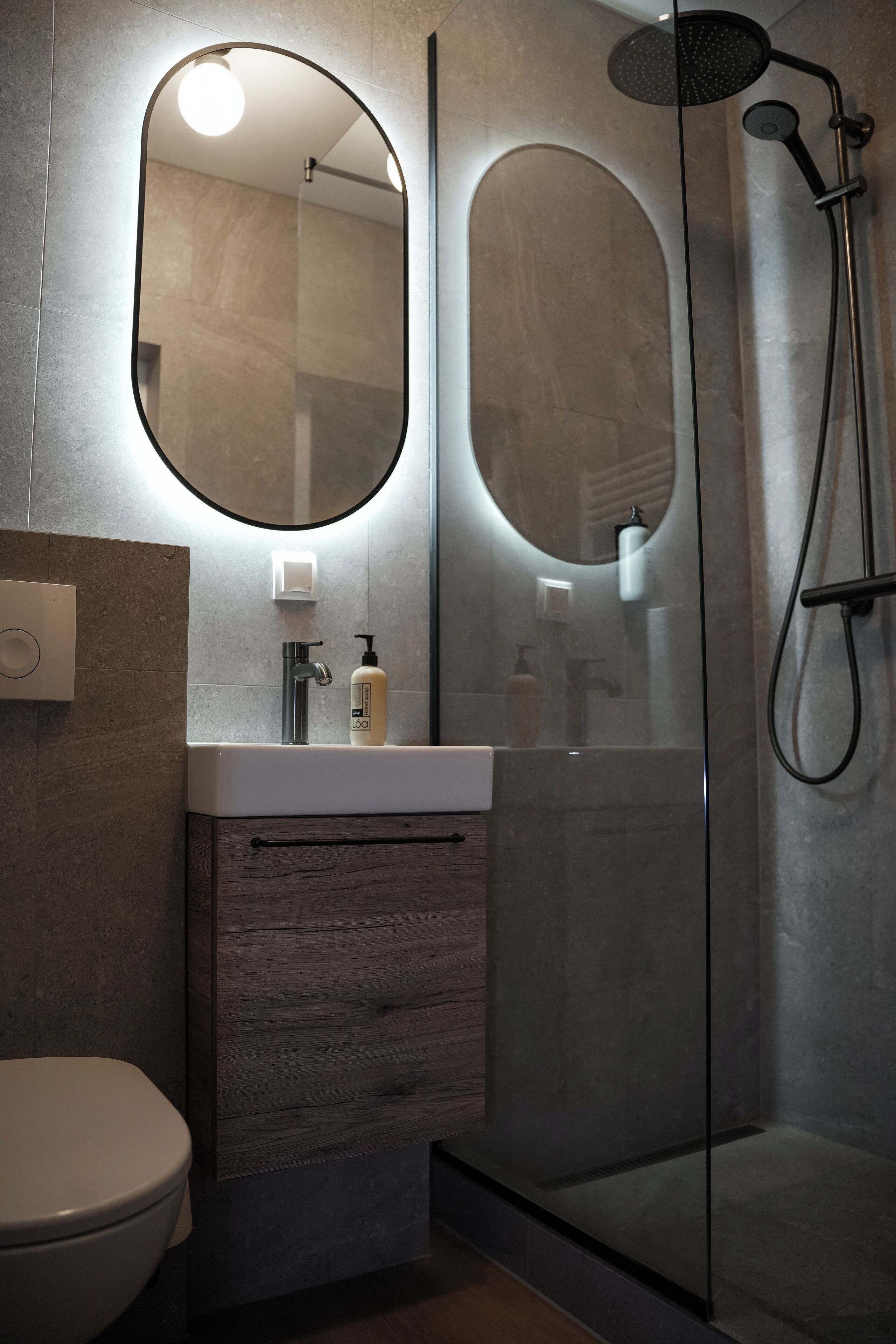 Un baño moderno con ducha de vidrio, un espejo redondo y un tocador de madera.
