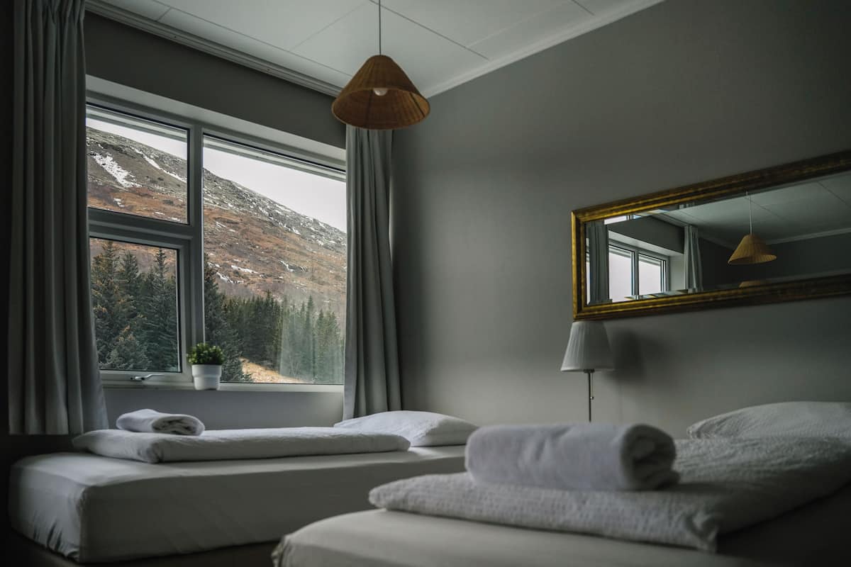 Een hotelkamer met twee bedden, een raam met uitzicht op een bergachtig landschap, een plant in een pot op de vensterbank en een hanglamp.