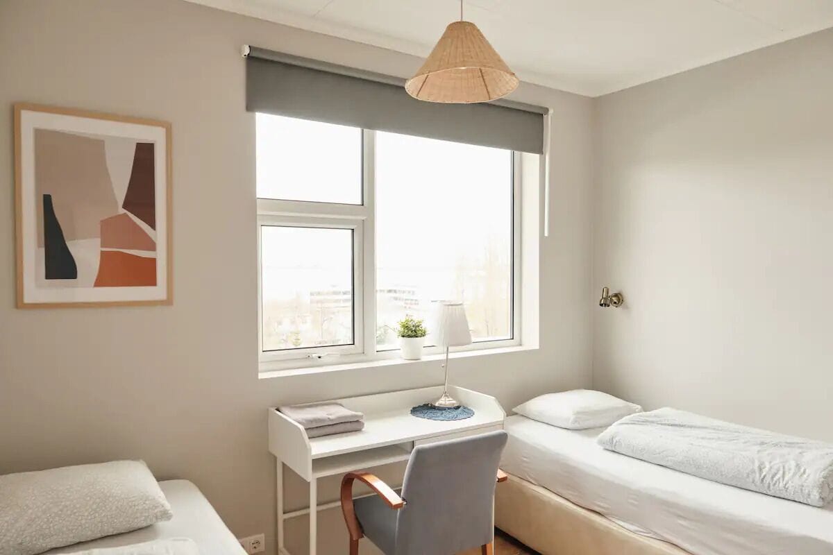 A modern bedroom with a desk, a chair, a bed, and a window with a view of the city.