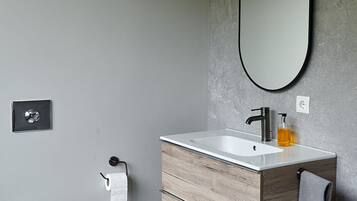 A modern bathroom with a white toilet, a wooden vanity with a white sink, and a large oval mirror.