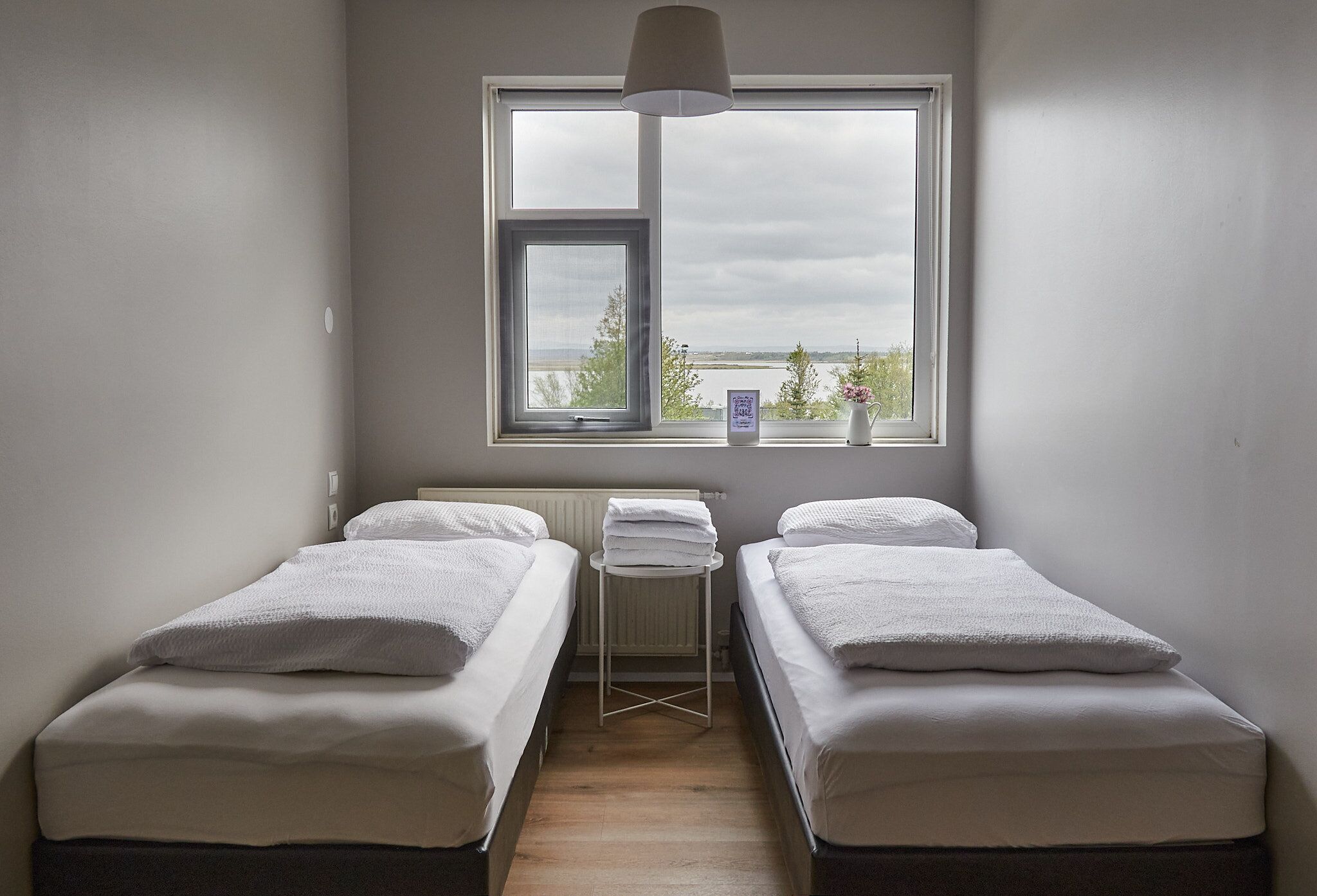 A room with two single beds, a window with a view, and a small table with towels.