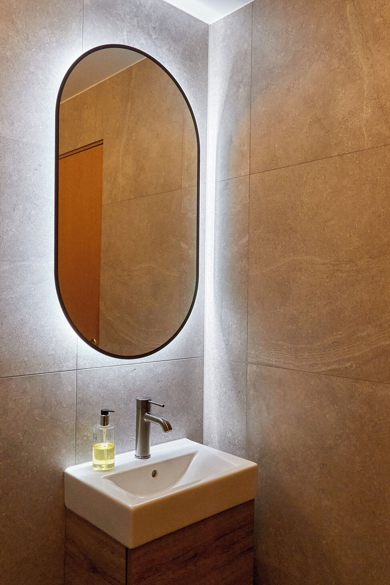 Un baño con un lavamanos rectangular, un grifo moderno y un espejo ovalado grande.
