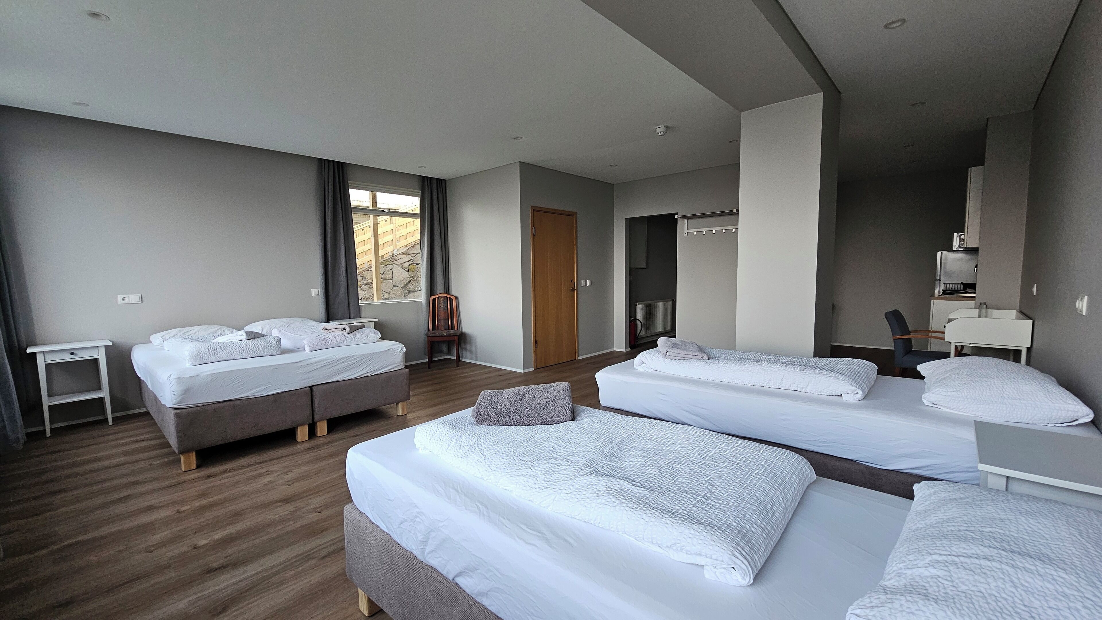 Habitación de hotel con dos camas, una mesita, una silla y un armario.