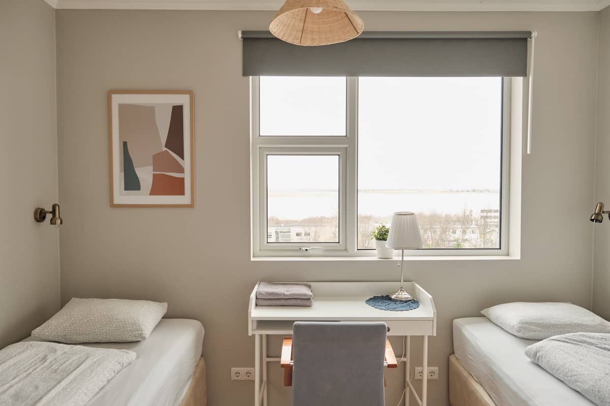 Een slaapkamer met twee bedden, een bureau en een raam met uitzicht.