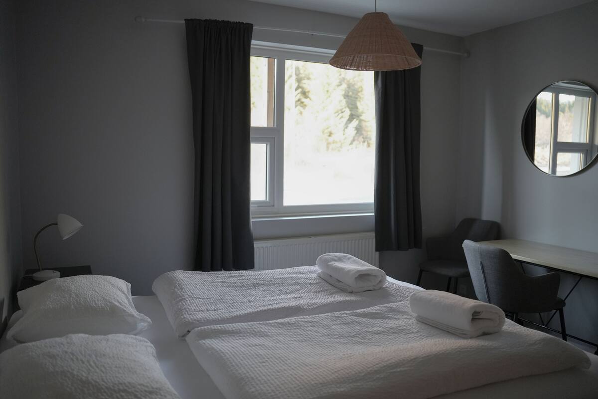 Een hotelkamer met een bed, een bureau, een stoel, een lamp en een raam met gordijnen.