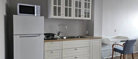 Een keuken met witte kasten, een roestvrijstalen koelkast, een magnetron, een spoelbak en een houten aanrecht.