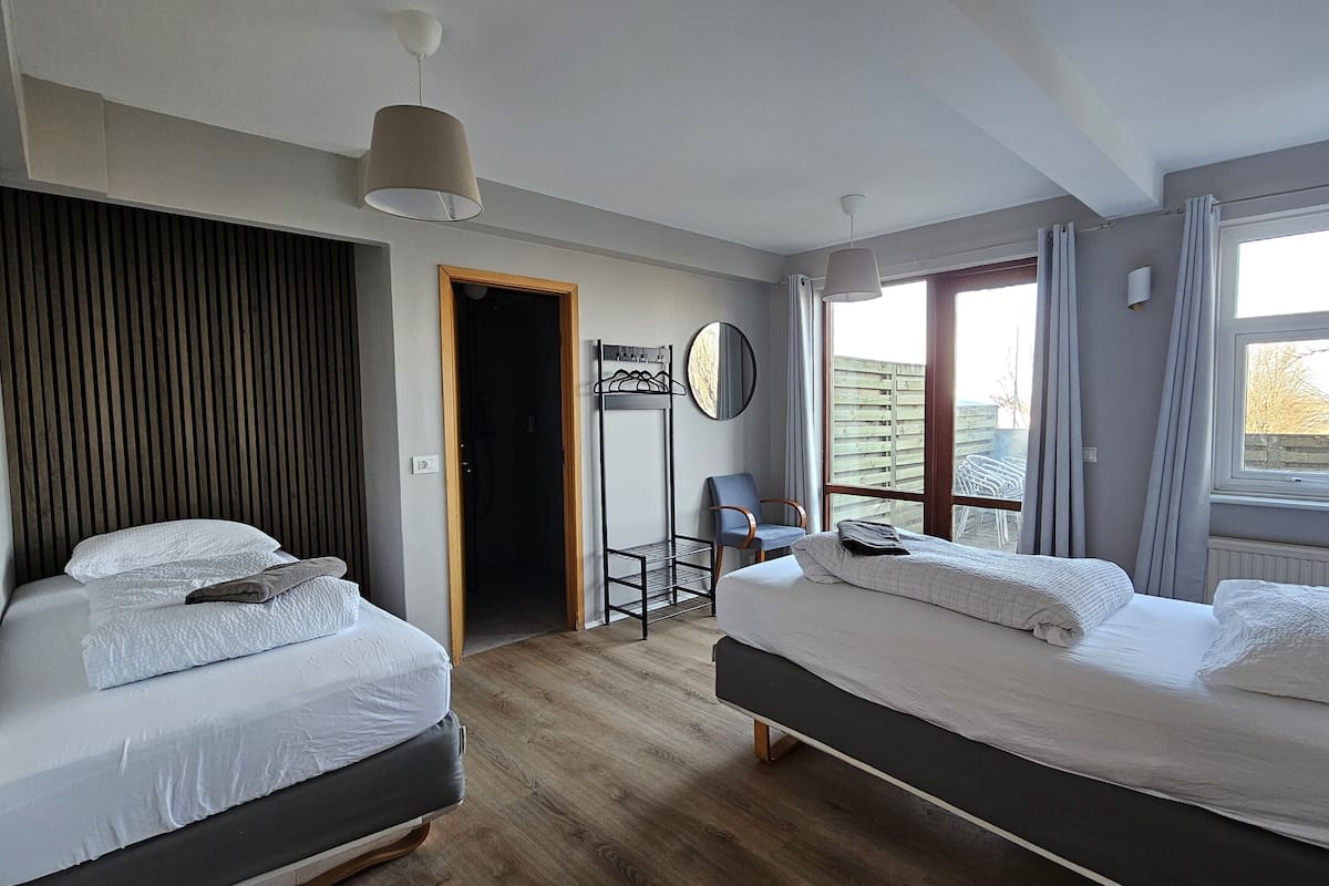 Een moderne hotelkamer met twee bedden, een houten vloer, een spiegel, een stoel en een raam met gordijnen.