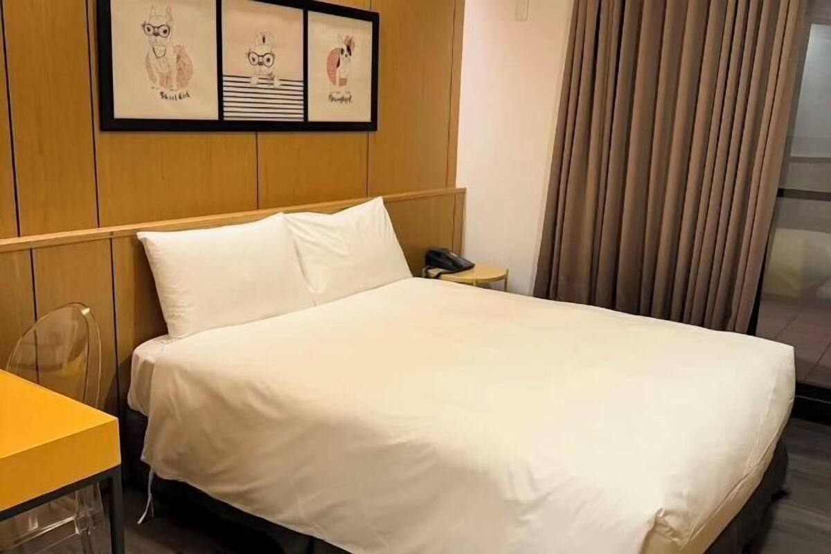 Ett hotellrum med en säng, ett nattduksbord med en telefon och inramade konstverk på väggen.