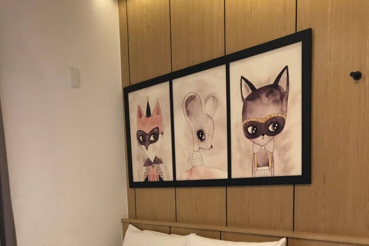 Ett hotellrum med en säng, ett nattduksbord med en telefon och en vägg med tre inramade bilder av djuransikten.