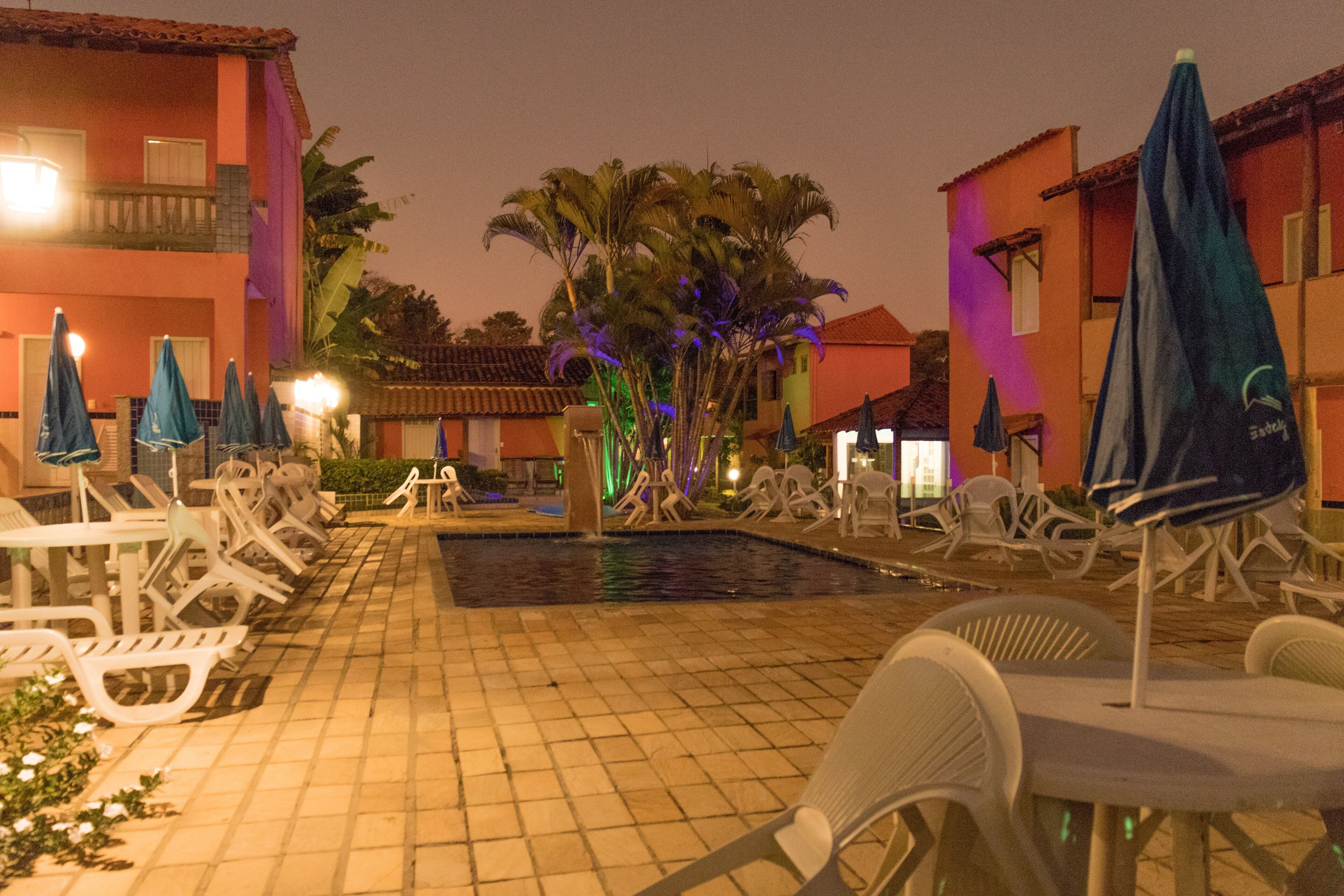 A pool area with lounge chairs and umbrellas, surrounded by buildings with balconies.
