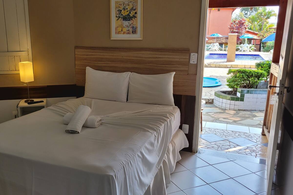 A neatly made bed with a white comforter and pillows, a bedside lamp, and a framed floral artwork on the wall.
