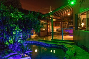 Zona exterior ben il·luminada amb piscina, envoltada de vegetació abundant i una zona de seients coberta.