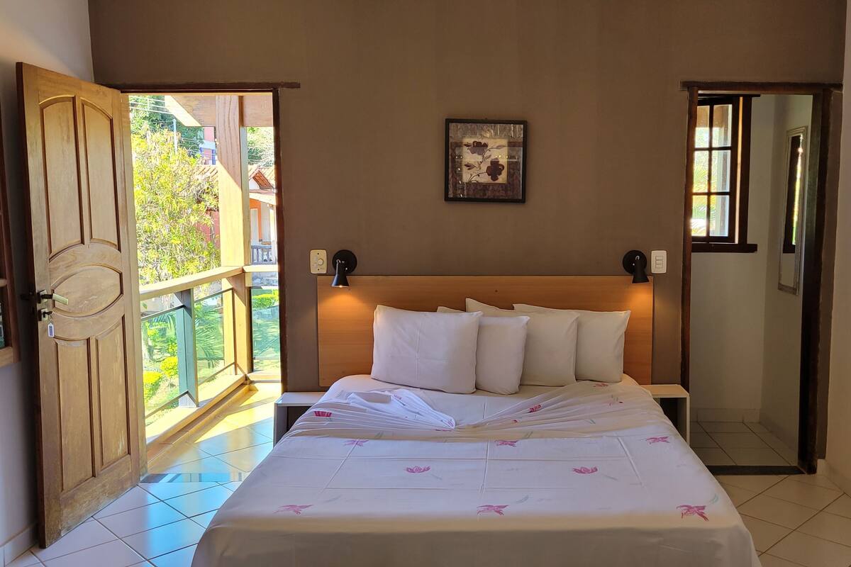 A bedroom with a bed, two wall-mounted lamps, a framed picture, and a window.