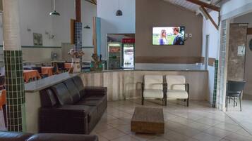 Restaurante com área de bar, mesas e cadeiras, e uma tela de televisão.
