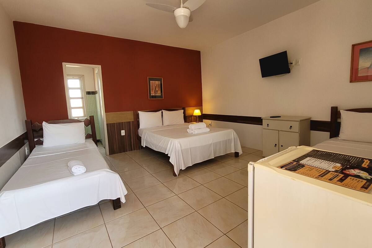 A hotel room with two single beds, a desk, a chair, a nightstand, a lamp, a television, and a framed picture on the wall.