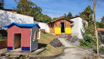 Two charming houses sit on a sloped terrain, surrounded by lush vegetation and a concrete pathway.