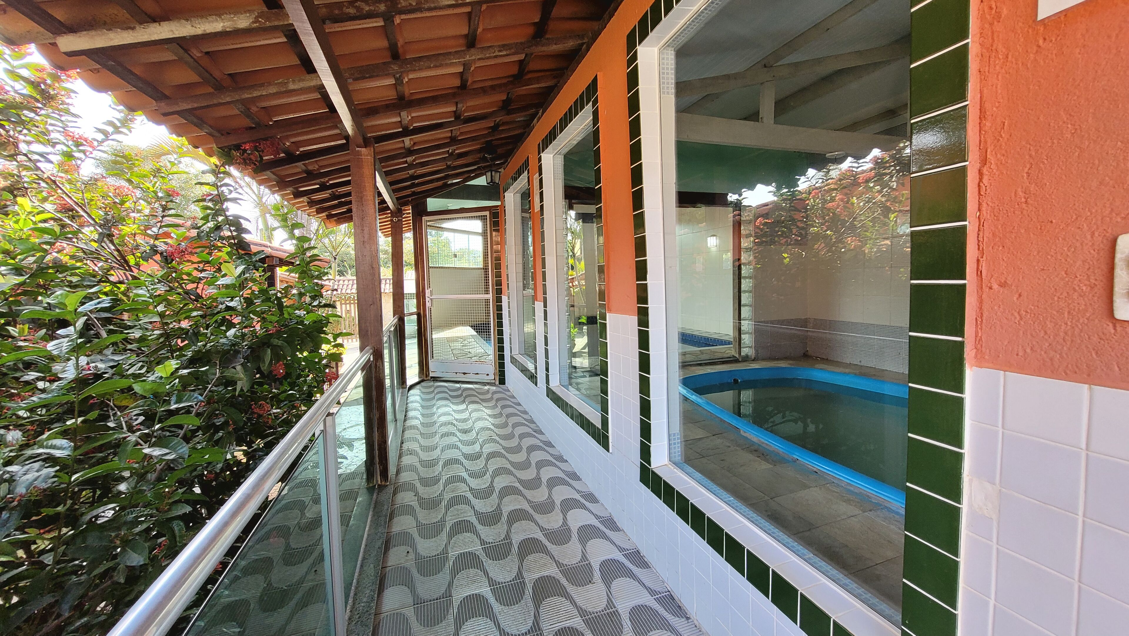 A covered outdoor area with a pool, glass railings, and a tiled floor.