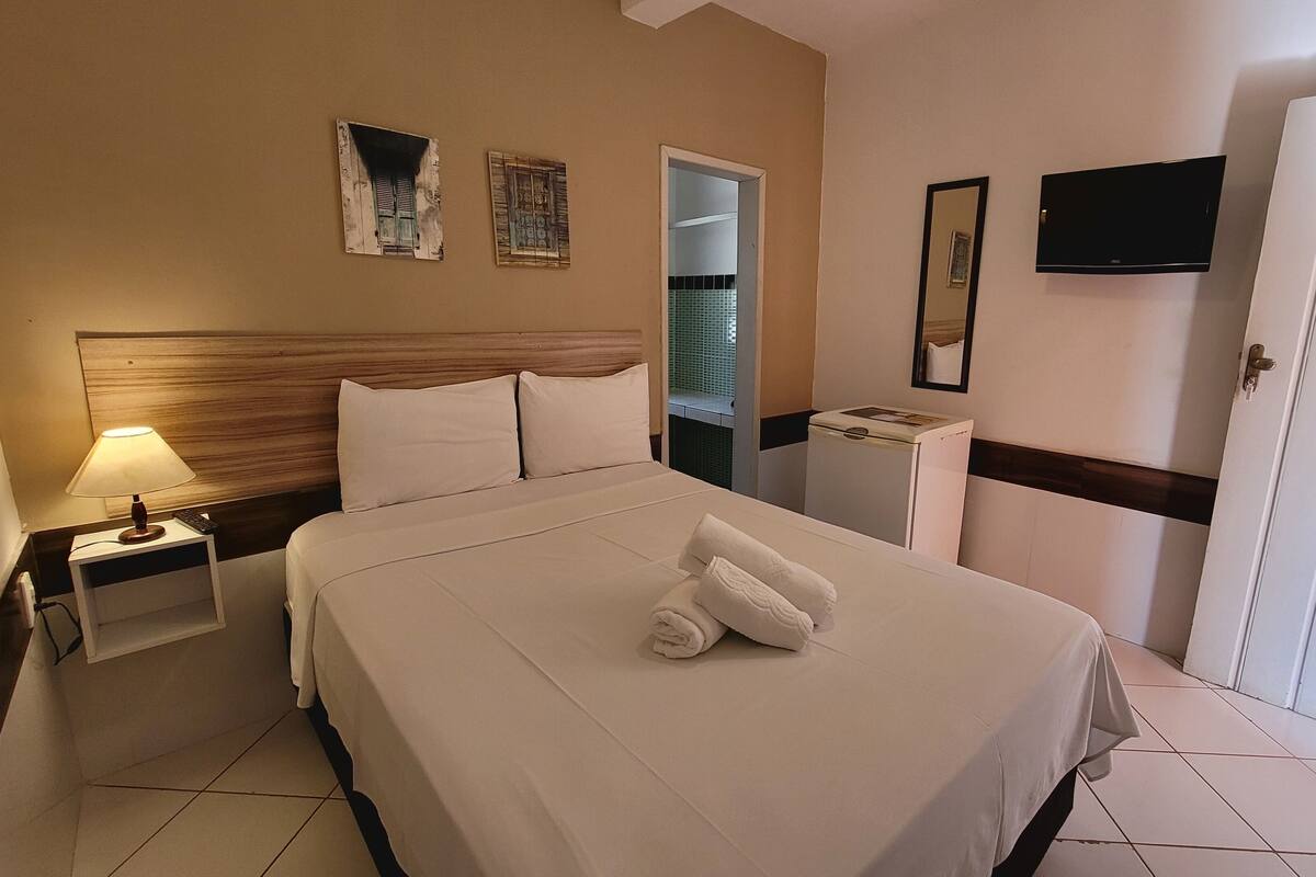 A hotel room with a bed, a nightstand, a lamp, a TV, and a door.