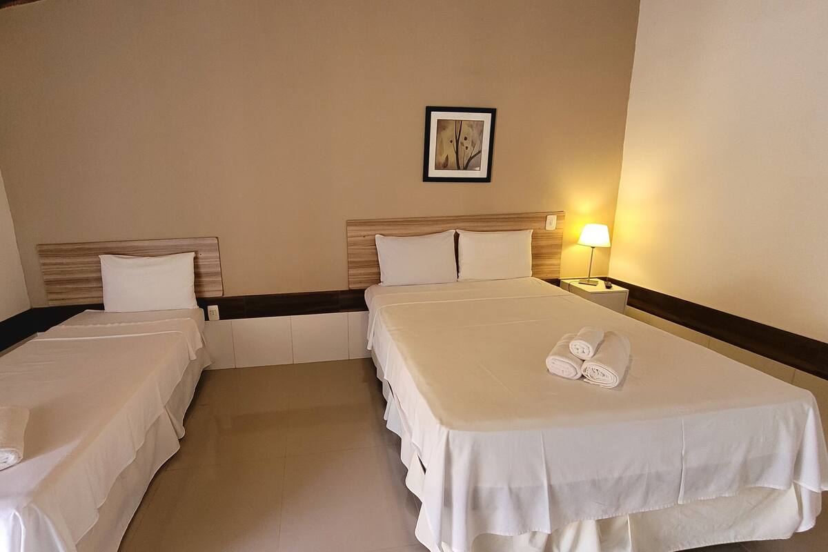 A hotel room with two single beds, a nightstand with a lamp, and a framed picture on the wall.