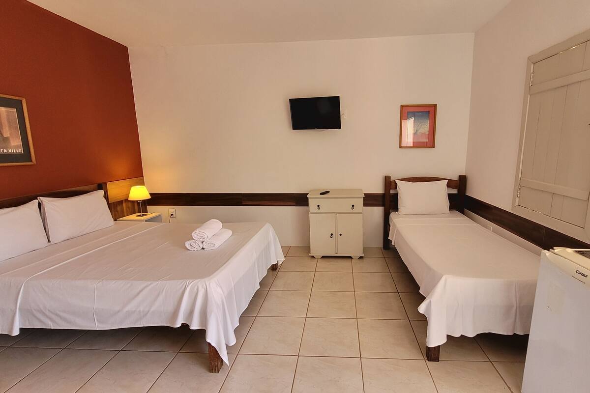 A hotel room with two beds, a TV, a small cabinet, and a refrigerator.