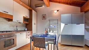 A compact kitchen with a stove, oven, and modern cabinets. There is a dining table with chairs and a small refrigerator. - Verona For Rent La Colombina (Verona)
