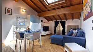 A modern living room with a dining area, wooden ceiling beams, a TV, and a sofa. - Verona For Rent La Colombina (Verona)