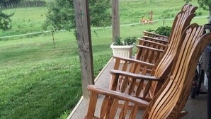 A wooden rocking chair on a porch with a view of a grassy field. - The Destination B&B (Salem)
