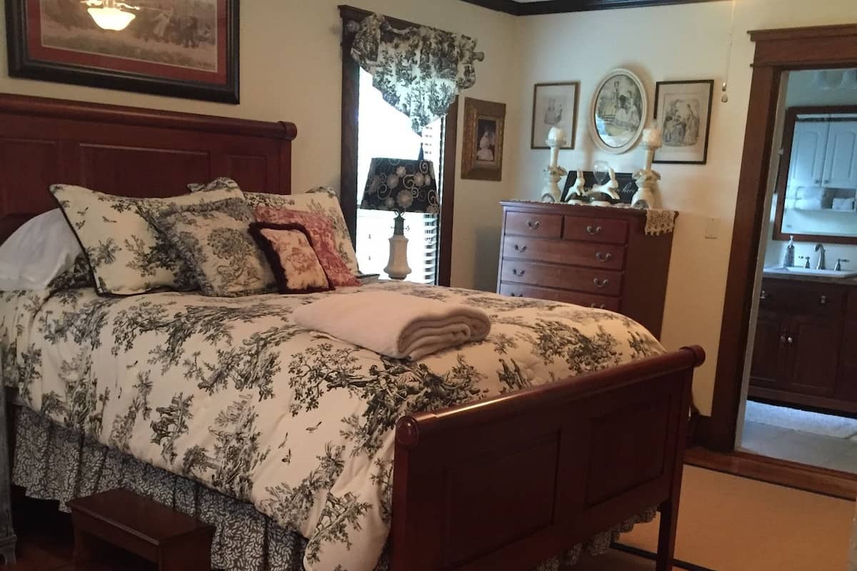 A bedroom with a wooden bed, a nightstand, a dresser, and a mirror.