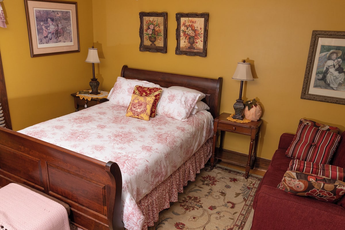 A neatly arranged bedroom with a wooden bed, a red sofa, and floral wall decorations.