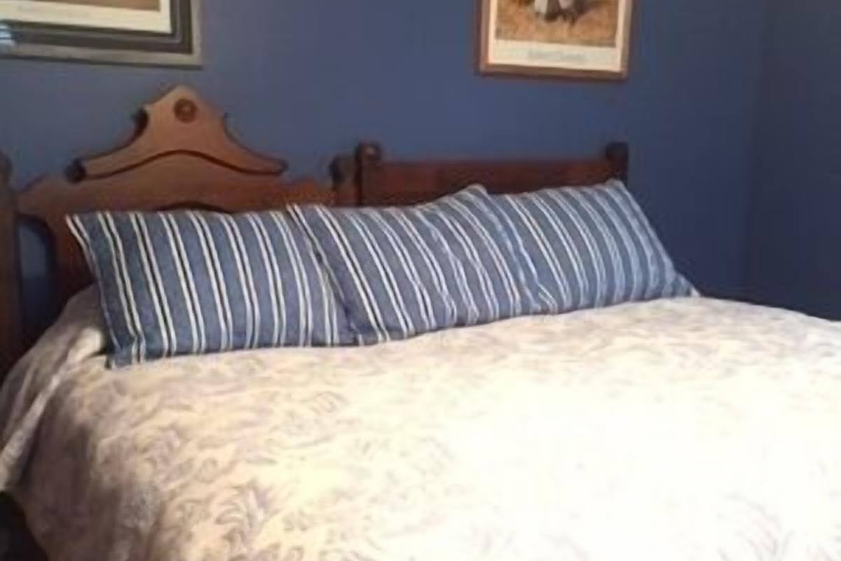 A bedroom with a wooden headboard, a floral patterned bedspread, and two striped pillows.