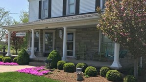 A two-story house with a covered porch, a stone fireplace, and a well-maintained garden with pink flowers. - The Destination B&B (Salem)