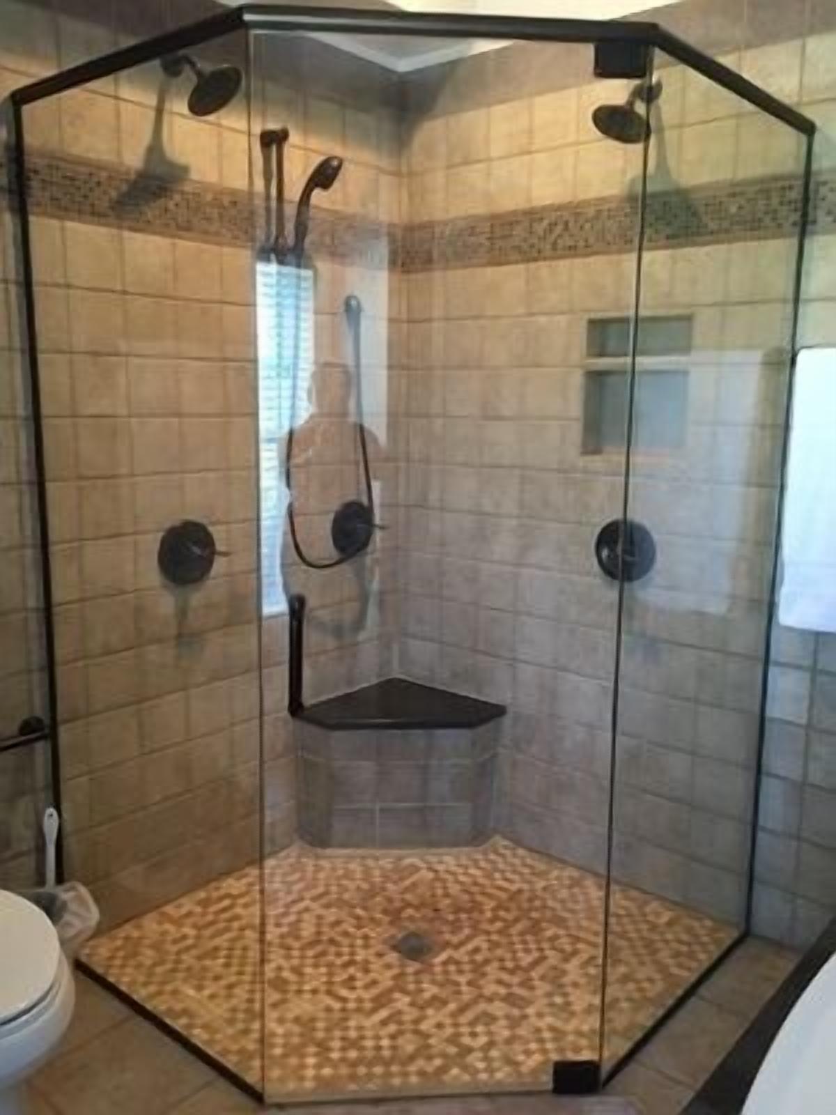 A glass-enclosed shower area with a tiled floor and a built-in bench.