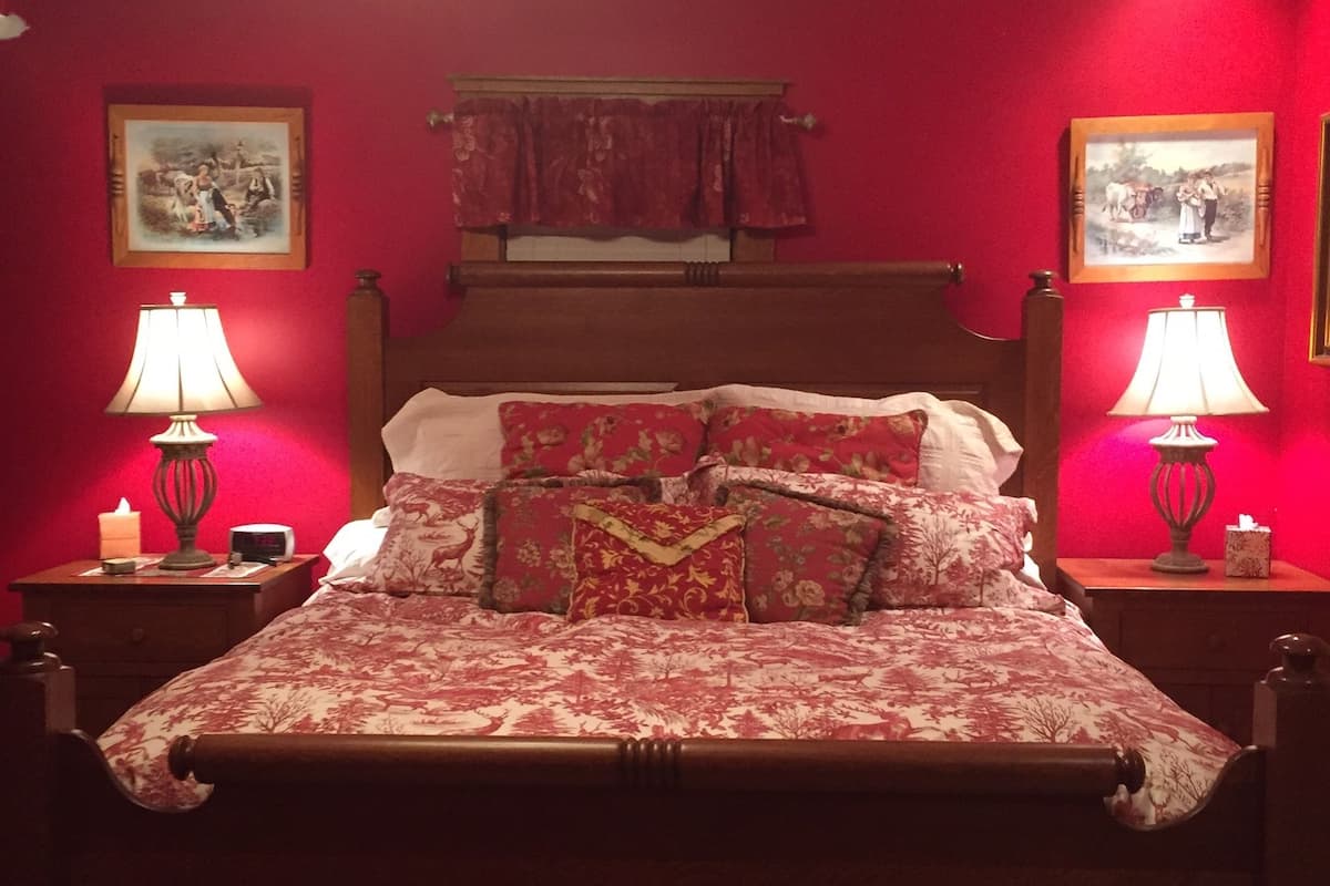 A traditional wooden bed with floral bedding, two bedside lamps, and a red wall with two framed pictures.